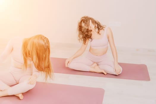 Young woman with long hair in white swimsuit and boho style braclets practicing outdoors on yoga mat by the sea on a sunset. Women's yoga fitness routine. Healthy lifestyle, harmony and meditation