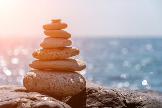 Balanced Pebbles Pyramid on the Beach on Sunny Day and Clear Sky at Sunset. Blue Sea on Background Selective focus, zen stones on sea beach, meditation, spa, harmony, calm, balance concept.