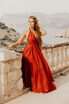 Woman red dress. Summer lifestyle of a happy woman posing near a fence with balusters over the sea