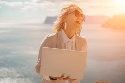 Freelance women sea. She is working on the computer. Good looking middle aged woman typing on a laptop keyboard outdoors with a beautiful sea view. The concept of remote work