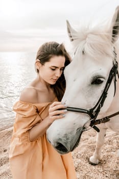 A woman in a dress stands next to a white horse on a beach, with the blue sky and sea in the background