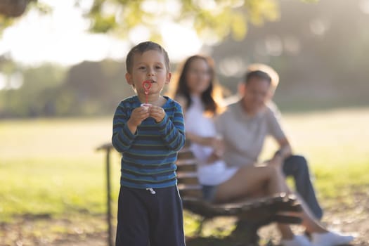 Cute little boy blowing soap bubbles with his parents behind his back. Mid shot