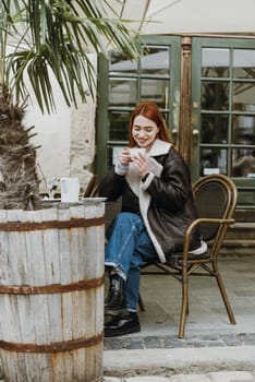 a red-haired girl in a leather jacket. great morning with coffee on the summer terrace in the cafe
