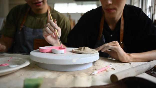 Cropped shot of young gay male couple painting pottery plate in workshop. LGBTQ, indoors lifestyle activity and hobbies concept.