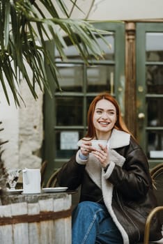 a red-haired girl in a leather jacket. great morning with coffee on the summer terrace in the cafe