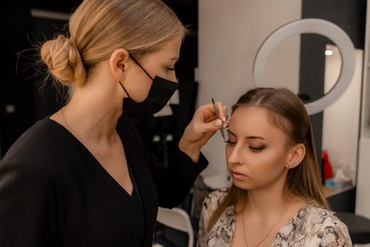 Makeup artist paints eyelashes to a woman in a beauty salon