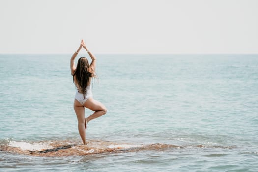 Woman sea yoga. Back view of free calm happy satisfied woman with long hair standing on top rock with yoga position against of sky by the sea. Healthy lifestyle outdoors in nature, fitness concept.