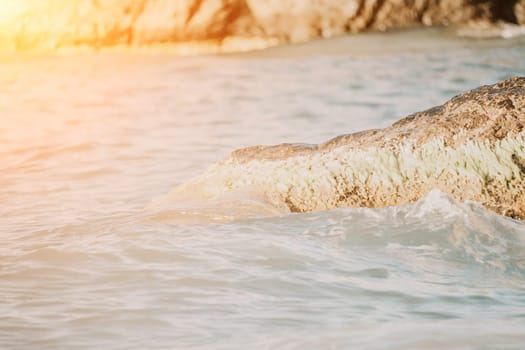 A red burning sunset with the silhouette of a cliff over the sea. Abstract nature summer or spring ocean sea background. Small waves on golden warm water surface with bokeh lights from sun.