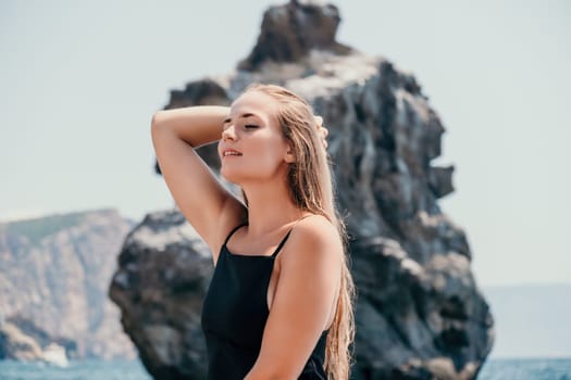 Woman travel sea. Young Happy woman in a long red dress posing on a beach near the sea on background of volcanic rocks, like in Iceland, sharing travel adventure journey