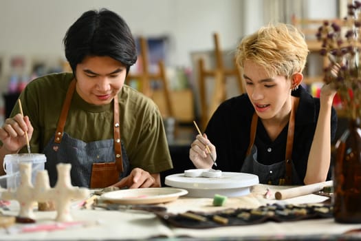 Handsome asian male ceramics art teacher helping a student with clay crafts in a pottery class. Art, handicraft and learning concept.