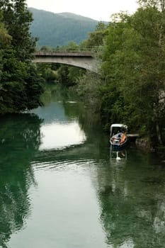 Small boat surrounded by lovely green trees at the Mangfall River with a bridge over it in Bavaria, Germany