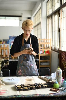 Young asian male sculptor in apron kneading clay for creating pottery ceramics. Handicraft, creativity and hobby concept.