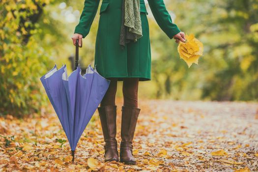 Woman in boots holding umbrella and fall leaves while standing in the park.
