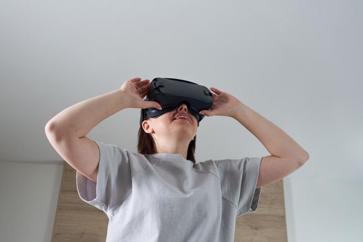 Happy young woman playing on VR glasses indoor. Virtual reality concept with young girl having fun with headset goggles.