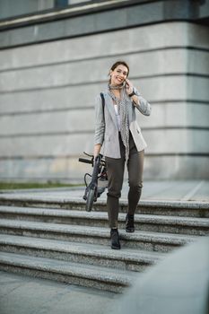 Shot of a young businesswoman talking on a smartphone while traveling with an electric scooter through the city.