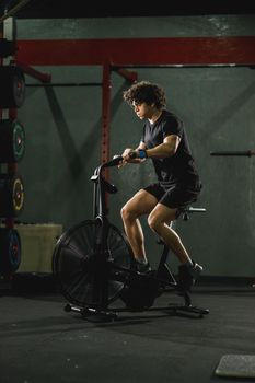 A muscular guy is doing hard cal bike crossfit training in the gym.