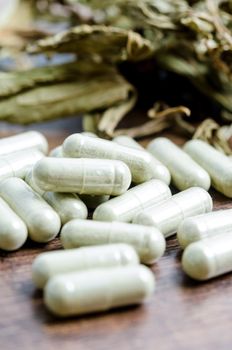 Pile of herbal medicine in capsules with herb dry leaf on wooden background.