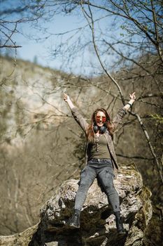 A smiling young woman sitting on the top of the mountain cliff and having fun the outdoors.