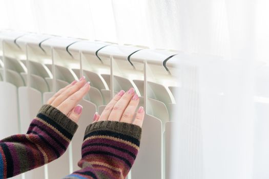 Girl warms up the frozen hands above hot radiator, close up