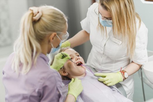 A female dentist examining cute little girl's teeth during dental procedure at dentist's office.