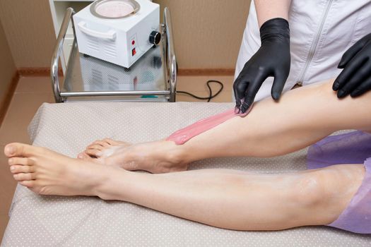 Cosmetologist beautician waxing female legs in the spa center beauty salon cosmetology concept