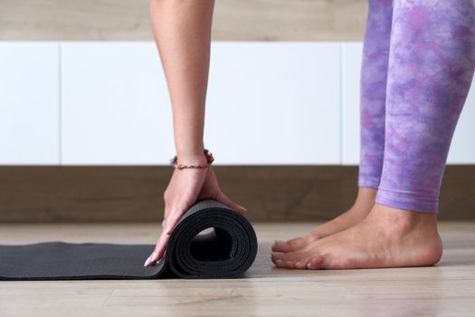 young woman folding black yoga or fitness mat after working out at home in living room