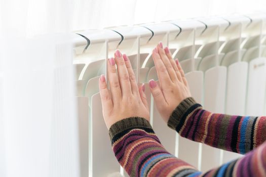 Girl warms up the frozen hands above hot radiator, close up