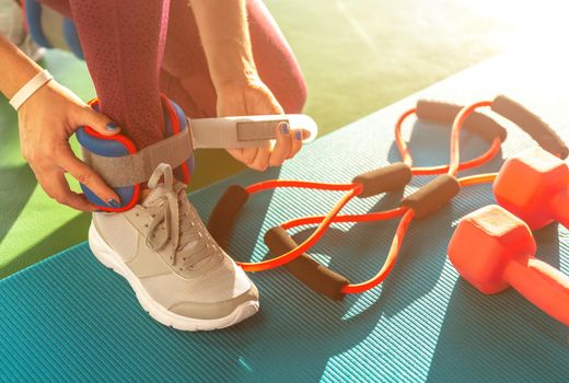 Woman putting on ankle wights before she starts a workout in a gym, health and fitness