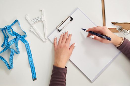 Nutritionist doctor writing diet plan on table with measuring tape, top view