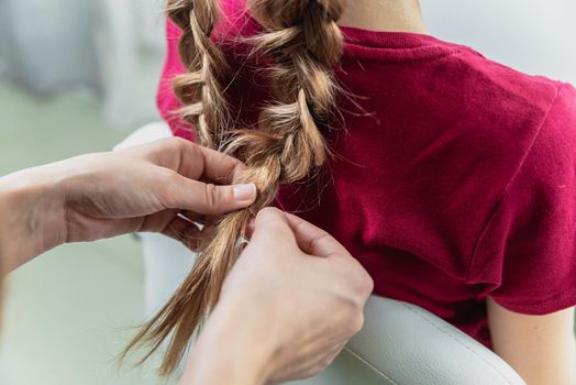 Hairdresser weaves a braid to a preteen blond girl