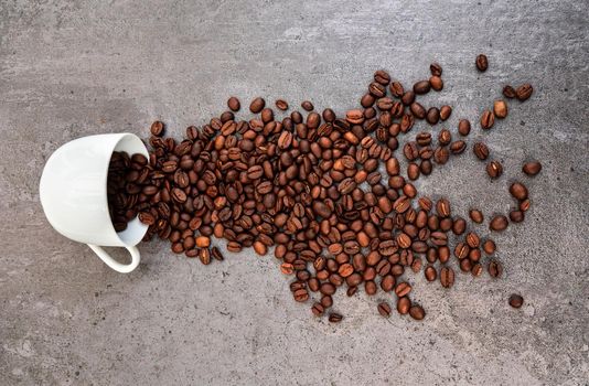 Spilled white cup of coffee with roasted beans scattered around