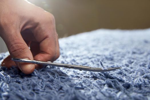 Closeup of hand cutting off string on a carpet with scissors