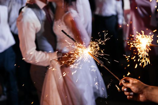 Sparkler in hands on a wedding - bride, groom and guests holding bright lights