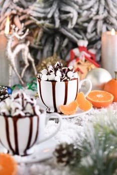 Hot chocolate with marshmallows in a white ceramic mug, with tangerines on a snowy table. The concept of a cozy holiday for Christmas and New Year.