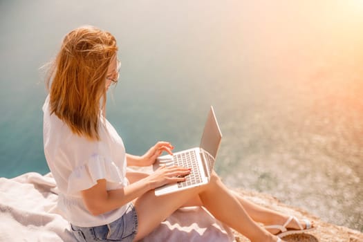 Freelance woman working on a laptop by the sea, typing away on the keyboard while enjoying the beautiful view, highlighting the idea of remote work