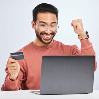 Laptop, credit card and man excited for online shopping, e commerce and payment in studio. Asian male person with technology and hand to celebrate savings win, promotion or sale on a fintech website.