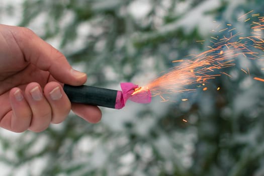 Burning Firecracker in a Hand. Guy Holding a Petard Outdoors in Winter at Daytime. Loud and Dangerous New Year's Entertainment. Hooliganism with Pyrotechnics. Noise of Firecrackers in Public Places