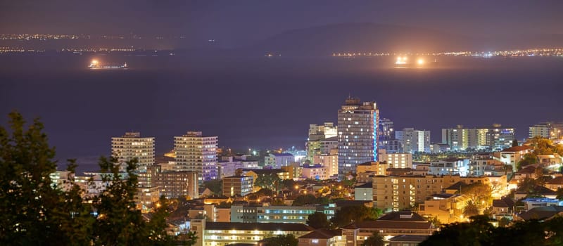 Harbour, buildings and city at night with lights, urban development and streets. Dark, travel and outdoor residential architecture of downtown with ocean or sea water in the evening with a skyline