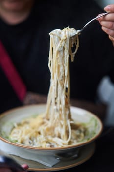 Appetizing carbonara paste with chicken improperly wound on fork. Spaghetti inaccurately hanging and falling from fork. Close up. High quality photo