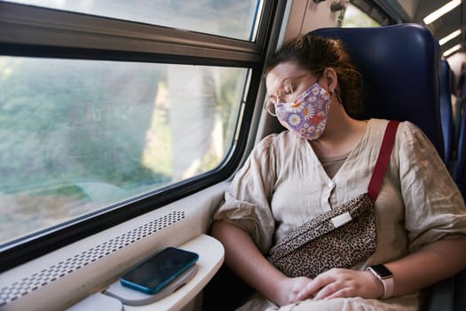 A girl with glasses in a medical mask sleeping on the train. High quality photo