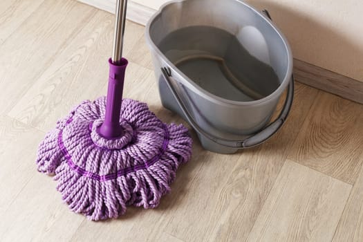 Purple mop on the floor with a bucket of water. The concept of indoor cleaning.