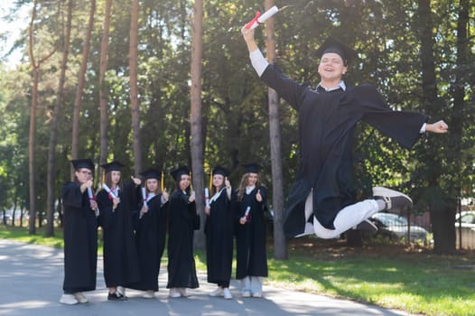 Happy young caucasian man celebrating graduation. Crowd of students graduates outdoors