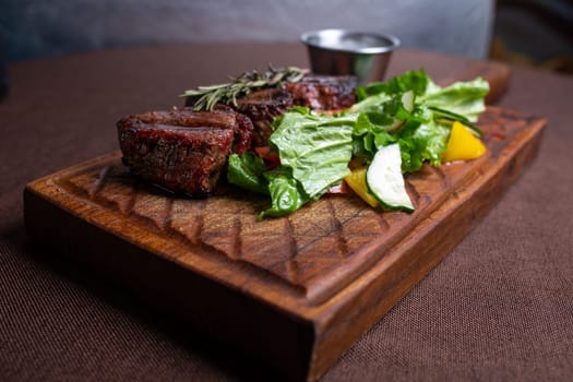 juicy beef steak with herbs and sauce on a wooden board.