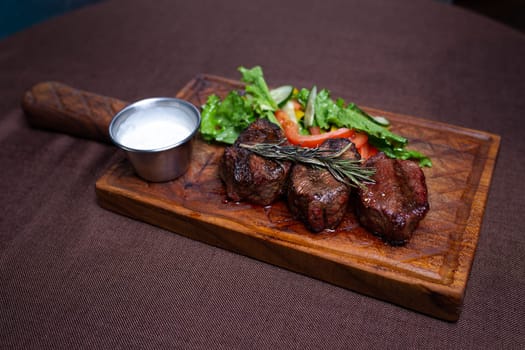 juicy beef steak with herbs and sauce on a wooden board.