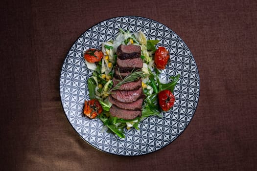 top view juicy sliced pieces of beef on a plate with herbs and tomatoes.