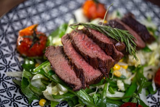 juicy cut piece of beef close-up on a plate with herbs and tomatoes.