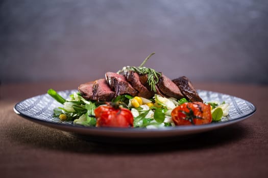 juicy sliced pieces of beef on a plate with herbs and tomatoes.