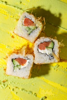 top view of Japanese cuisine rolls with fish, cucumber and cheese on a yellow background.