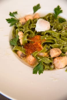 close-up of green pasta with salmon and red caviar and greens in a white plate.