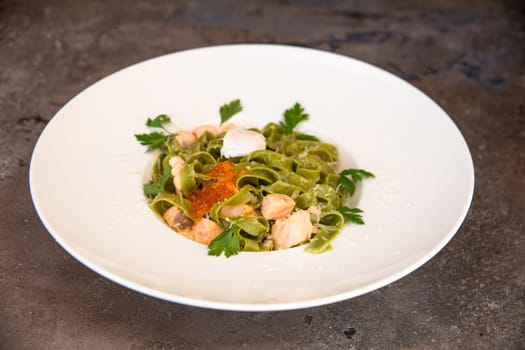 green pasta with salmon and red caviar and greens in a white plate.